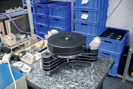 Gramofon Innovation przygotowany do finalnych prac montażowych; napęd oraz platforma mogą przyjąć ramiona o różnej konstrukcji (w niebieskich skrzyniach za stołem montażowym).